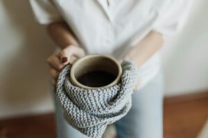 woman holding ceramic mug in knitted towel