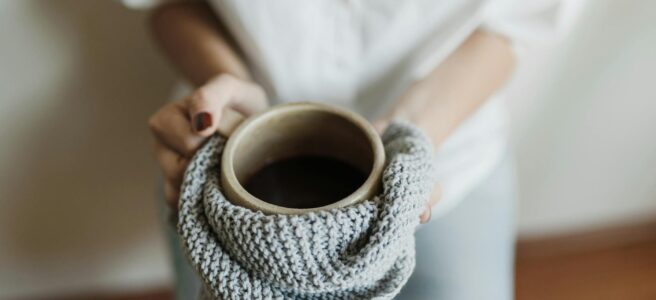 woman holding ceramic mug in knitted towel